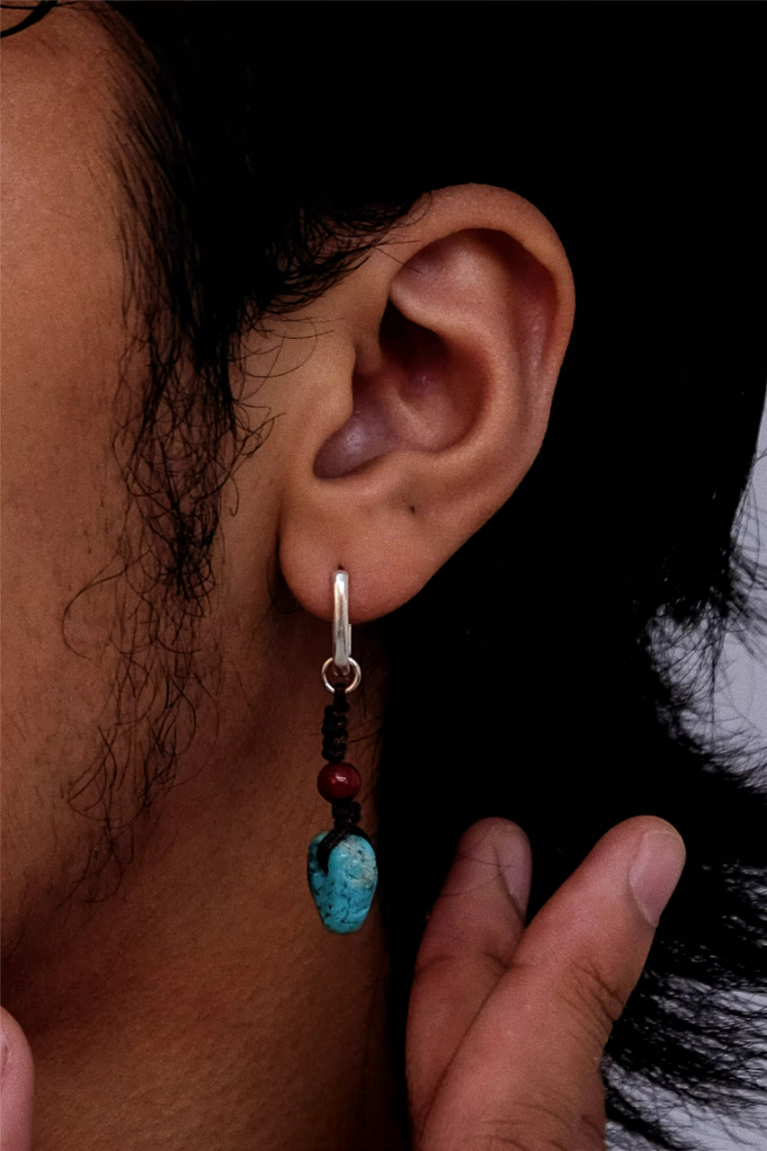 A silver hoop earring with hand-knotted turquoise and cinnabar dangles on an ear.
