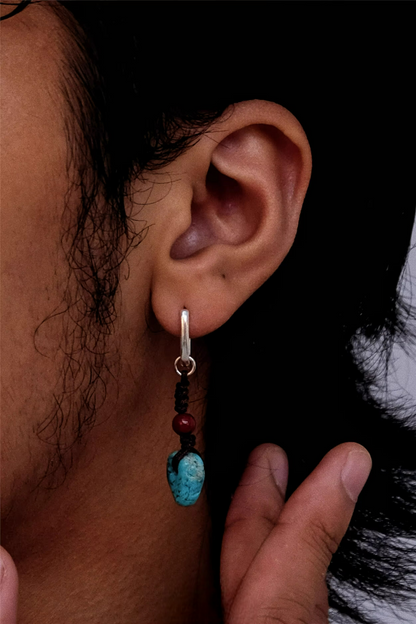 A silver hoop earring with hand-knotted turquoise and cinnabar dangles on an ear.