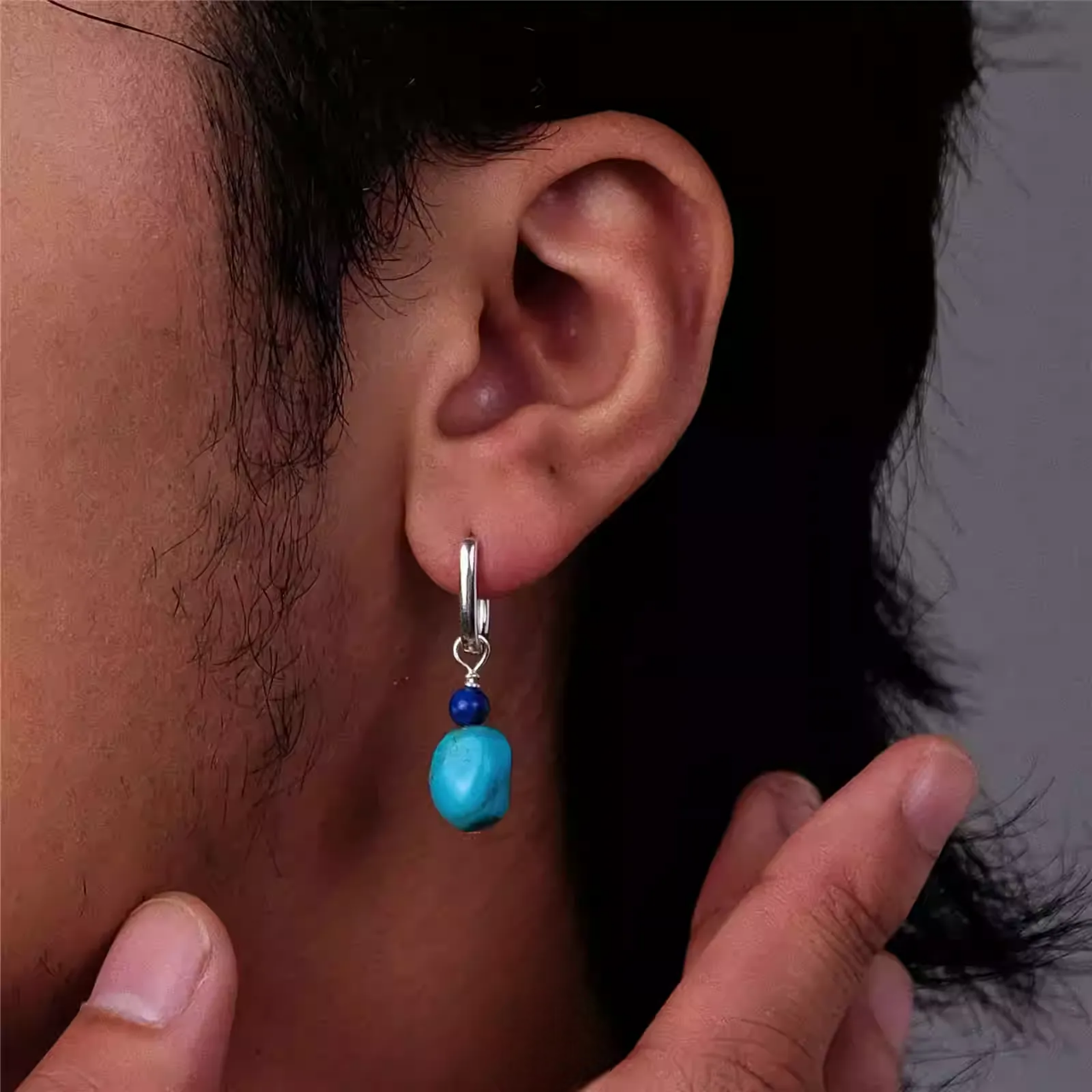A silver hoop earring with lapis lazuli and raw turquoise beads on an ear.