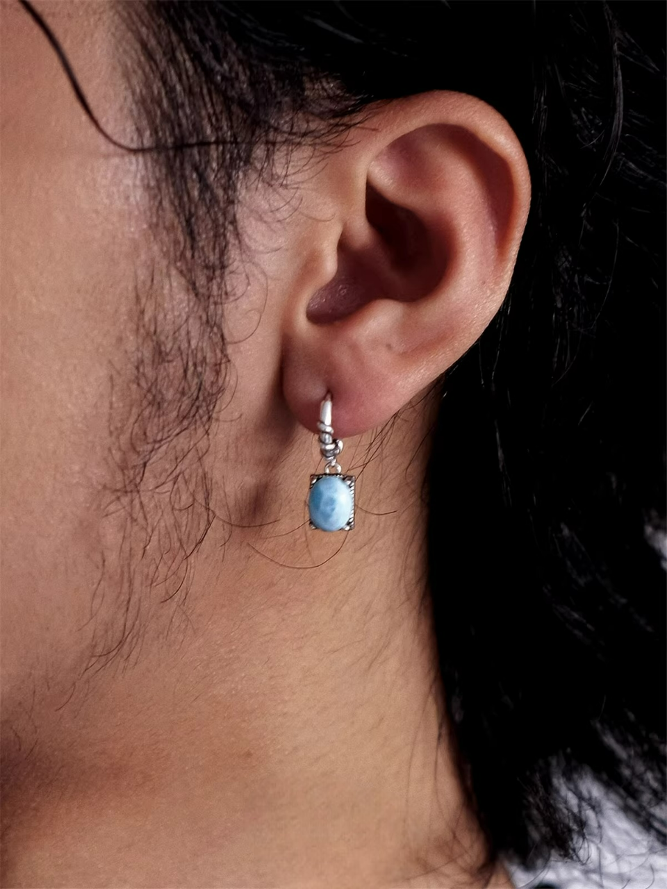 Vintage silver huggie earring with a light blue larimar stone on a person's ear.