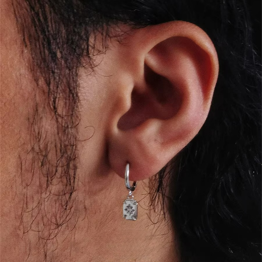 Silver huggie earring with a rectangular drop charm featuring a star design.