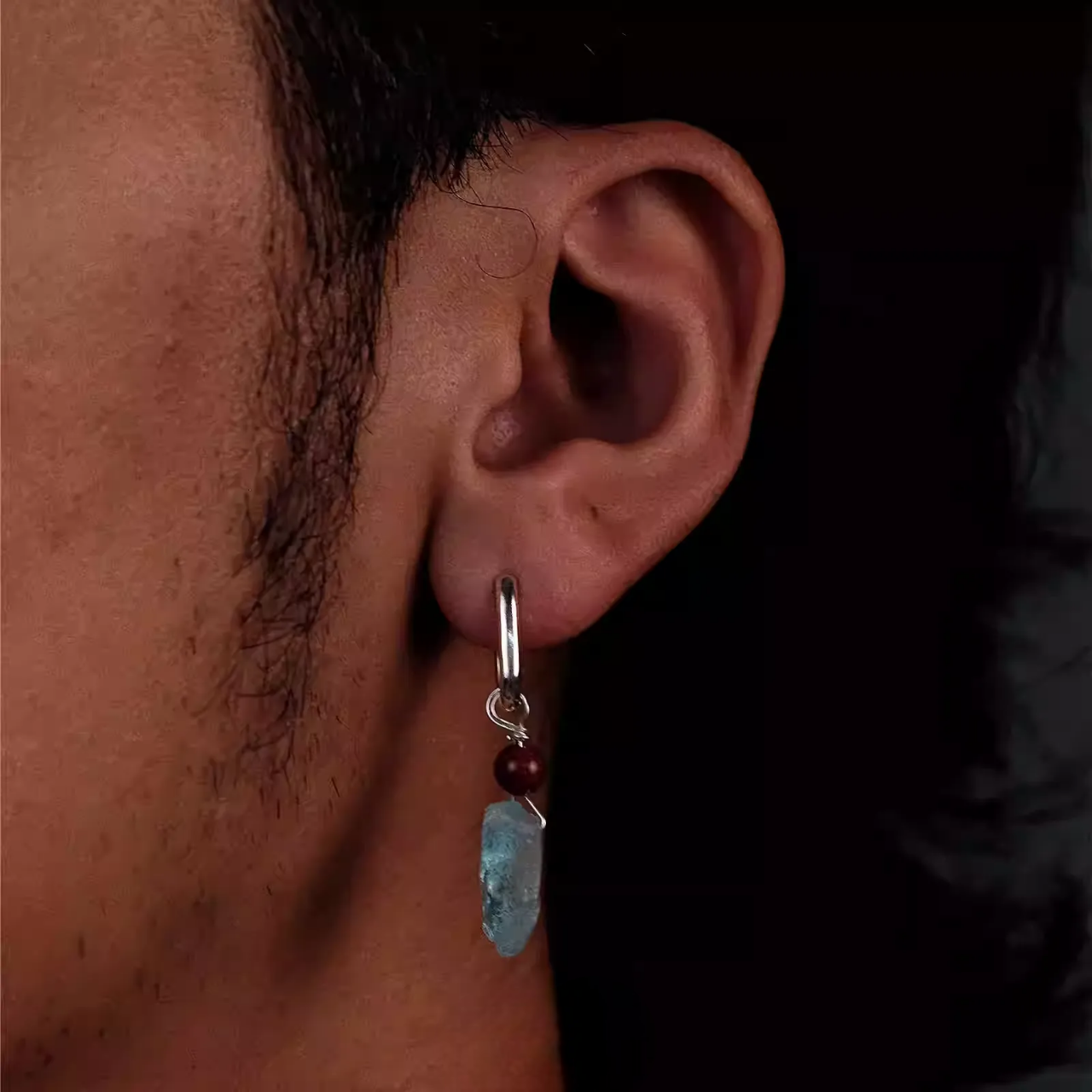 A silver hoop earring with a red bead and raw blue aquamarine stone.