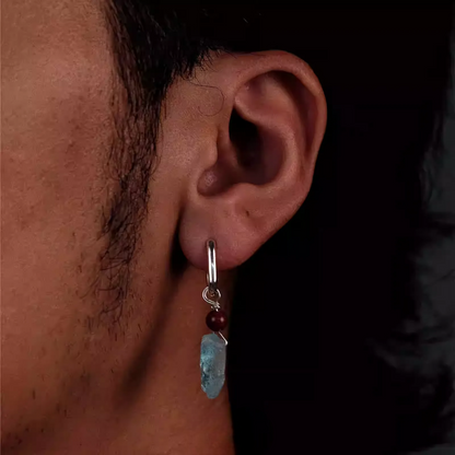 A silver hoop earring with a red bead and raw blue aquamarine stone.