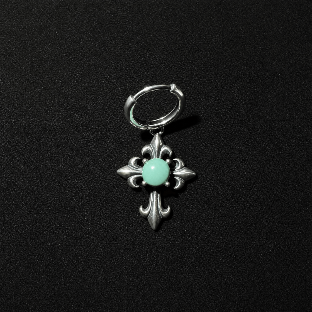 Unisex gothic punk S925 silver huggie earrings featuring a turquoise cross dangle, resting on a textured dark stone surface
